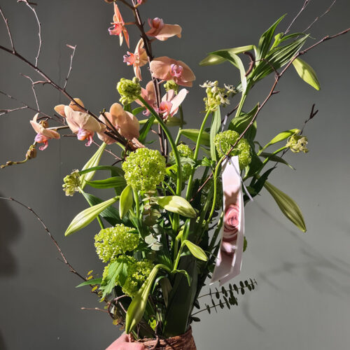Een Staf boeket met bloemen, met licht roze bloemen en veel groene takken. Het boeket is aan de onderkant bij elkaar gebonden.
