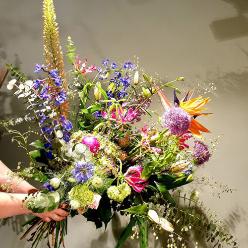 Een groot boeket met verschillende soorten paarse, oranje en roze bloemen, met groene takjes erdoorheen